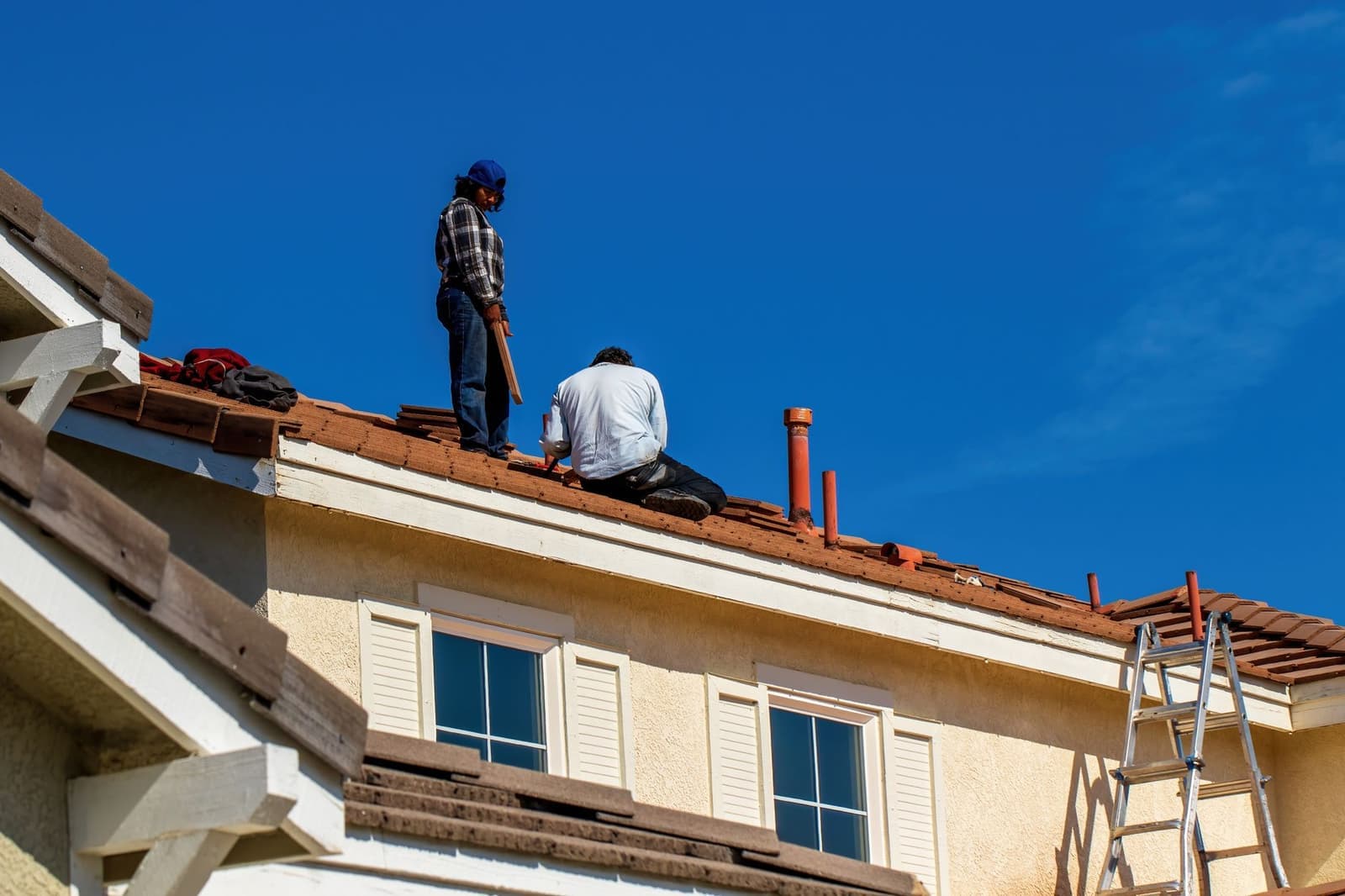 Workers on a tile roof beside a ladder
