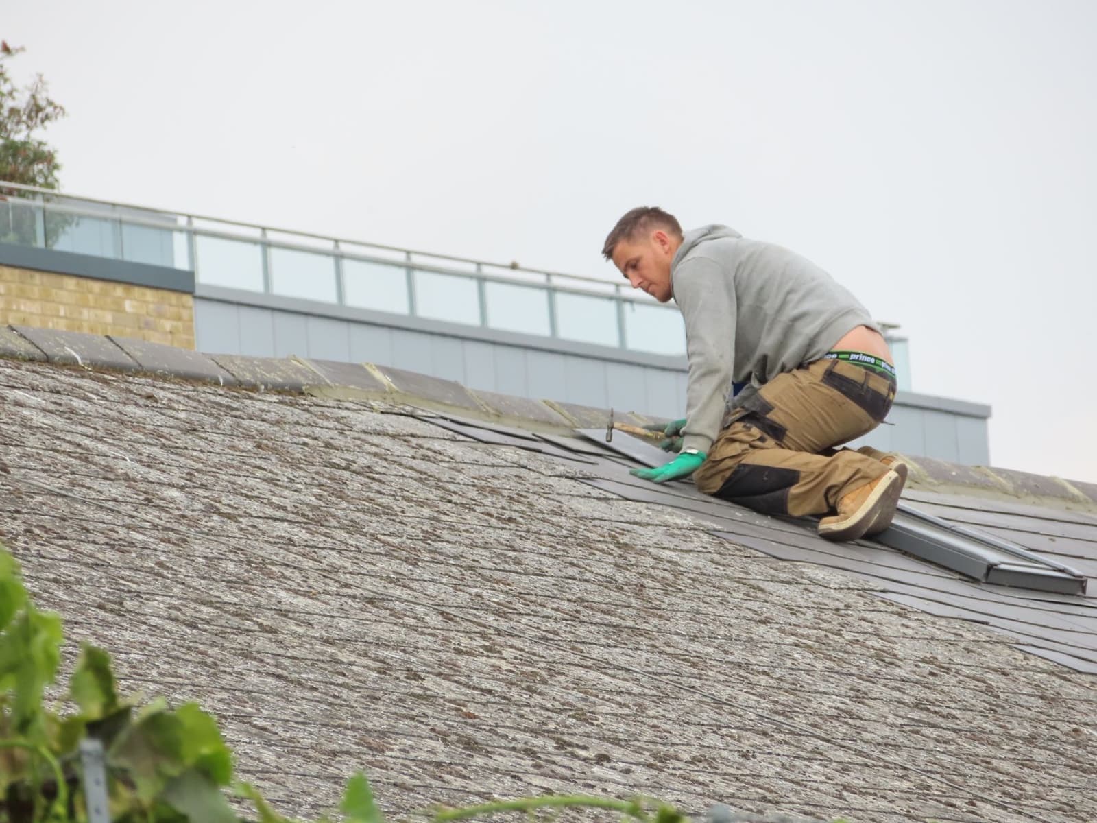 Roofer kneeling on a gray shingle roof